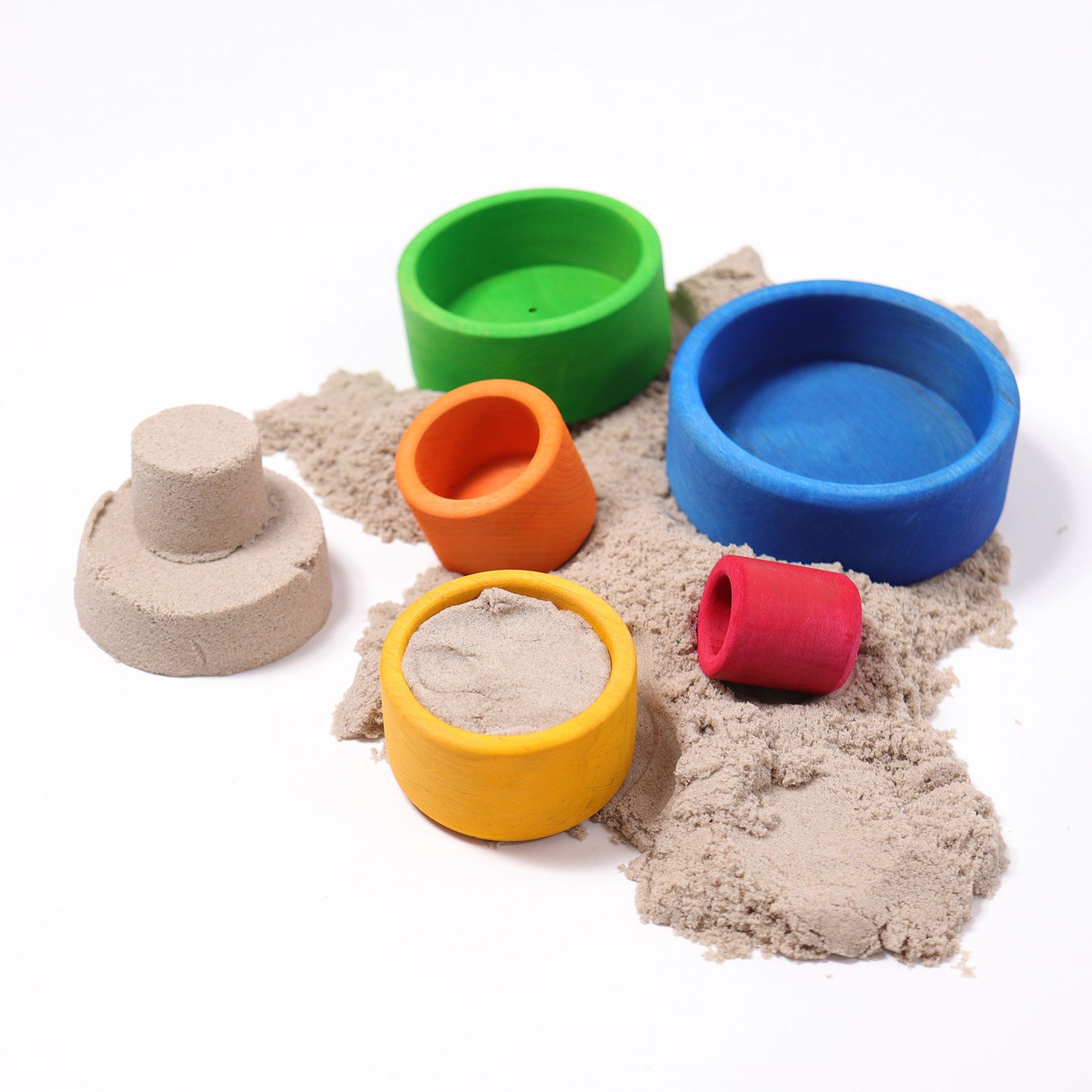 Five bright rainbow wooden bowls are scattered amongst play sand. A sandcastle has been built using two of the bowls as a mold.