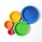 Wooden nesting bowls in various sizes are set out, they are bright rainbow coloured.